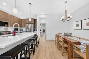 A modern kitchen with a central island, bar stools, and a dining area with a wooden table and chairs. - 106 Homestead Loop Luxury 3 bedroom, mt view, private patio, outdoor HT (Fraser)