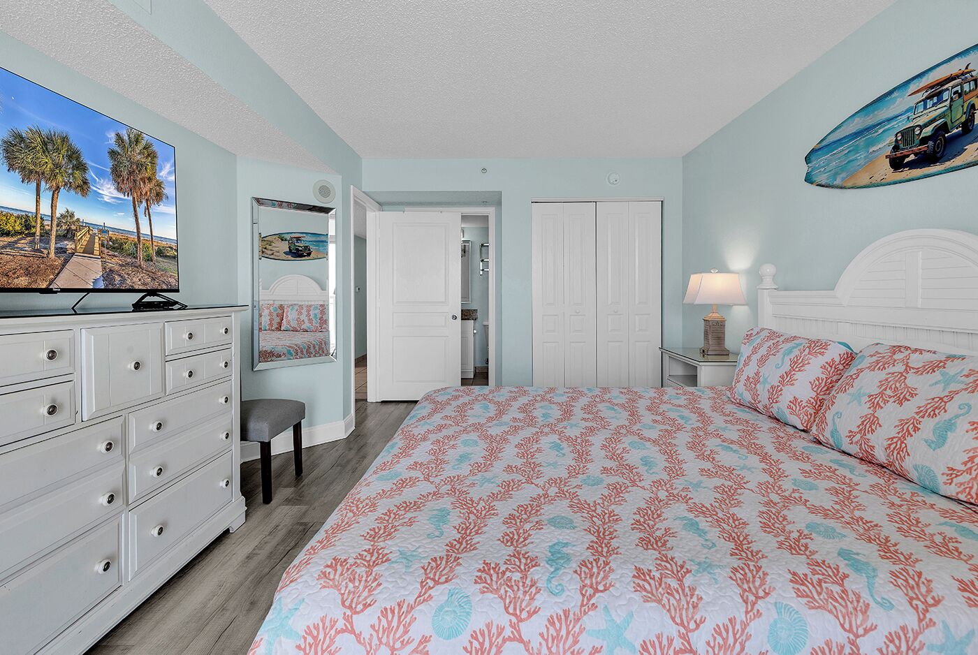 A bedroom with a bed, dresser, mirror, and a door leading to another room.