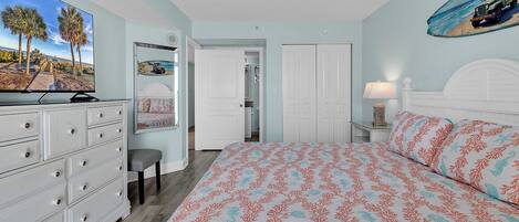 A bedroom with a bed, dresser, mirror, and a door leading to another room.