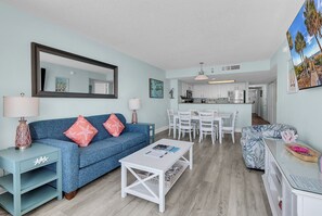 A living room with a sofa, coffee table, and dining area with chairs. - Baywatch Resort l 3BR l Top Floor l Resort Pools (North Myrtle Beach)