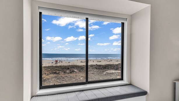 A room with a large window overlooking a beach, a built-in bench, and a radiator. - Newly Renovated Oceanfront 3BR at Sea Cloister ll | Cherry Grove (North Myrtle Beach)
