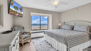 A bedroom with a bed, a desk, a chair, a TV, a ceiling fan, a window with a beach view, and a rug. - Newly Renovated Oceanfront 3BR at Sea Cloister ll | Cherry Grove (North Myrtle Beach)