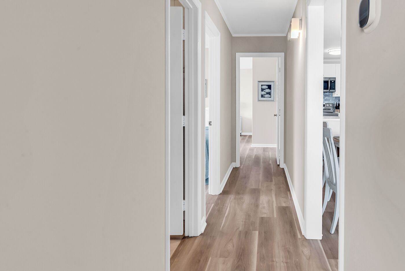 A hallway with a wooden floor, white walls, and a door at the end leading to a kitchen area.