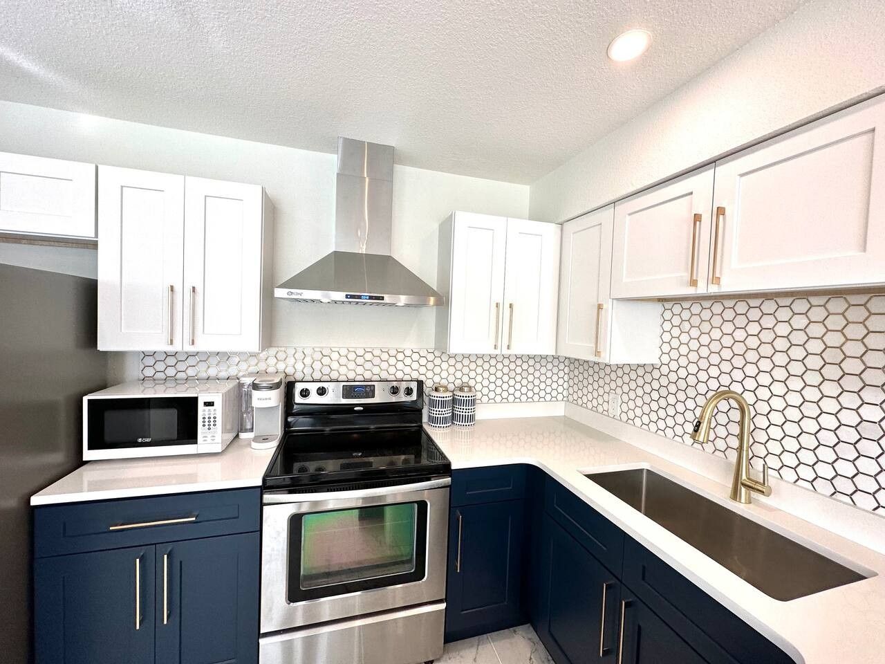 A modern kitchen with stainless steel appliances, white cabinets, and a hexagonal tile backsplash.