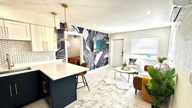A modern kitchen with a marble countertop, a dining area with a round table, and a living space with a sofa and a plant. - Stunning 1 brm: beach across street, port 8 mi, Ron Jon 4 mi, nightlife 1.6 mi (Cocoa Beach)