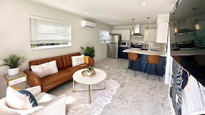 A modern living room with a brown sofa, a white coffee table, and a kitchen area with a bar. - Stunning 1 brm: beach across street, port 8 mi, Ron Jon 4 mi, nightlife 1.6 mi (Cocoa Beach)