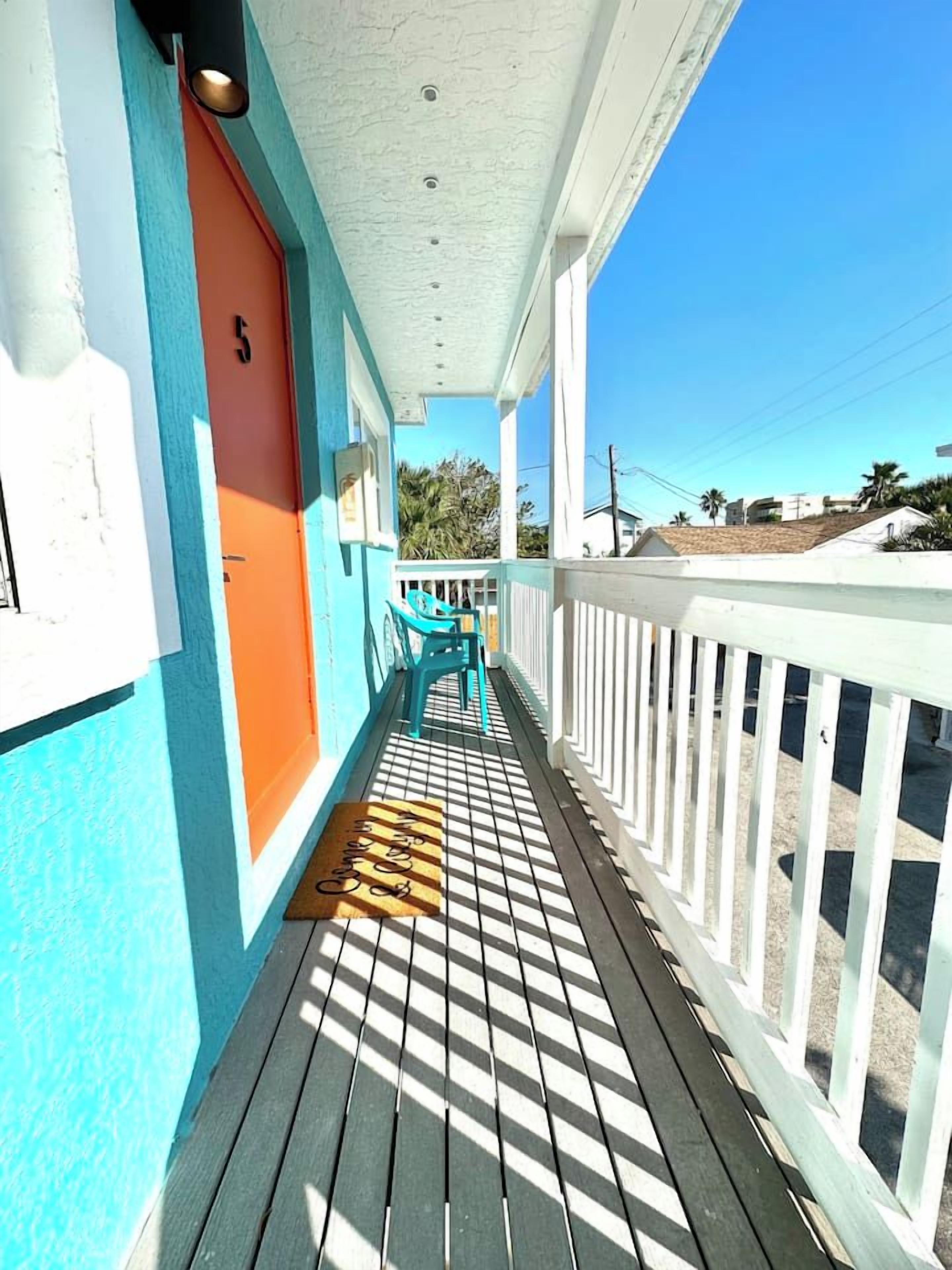 A wooden deck with a white railing, a door with a number, and a bench.