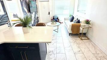 A modern kitchen with a marble countertop and a built-in island, a dining area with a round table, and a living space with a sofa and a coffee table.