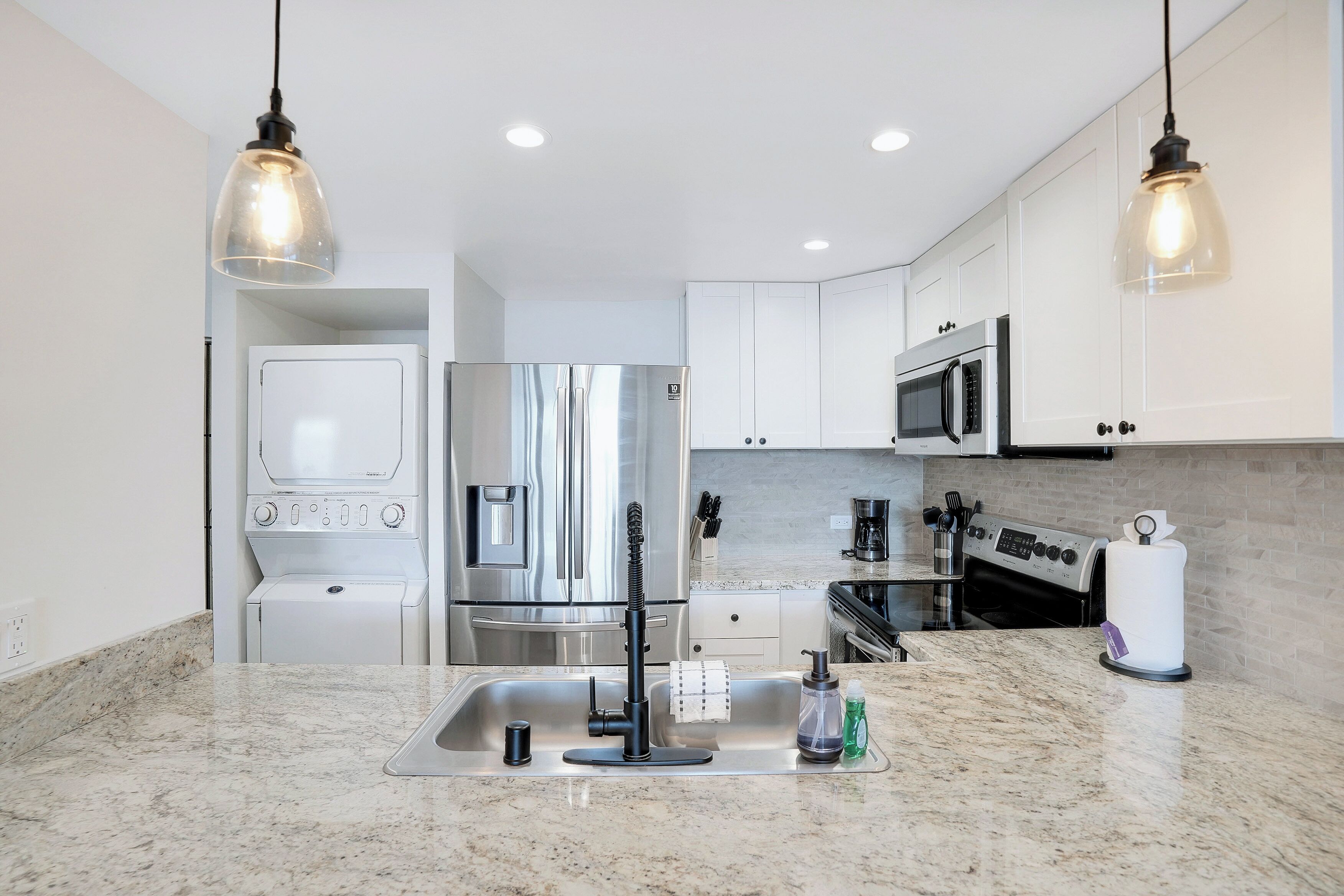 A modern kitchen with stainless steel appliances, a granite countertop, and pendant lighting.