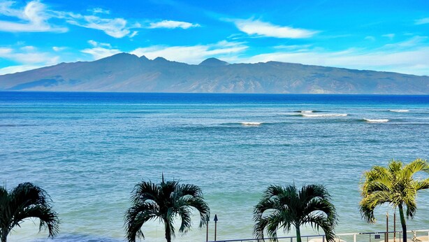 A coastal view with a mountain range in the background, palm trees in the foreground, and a clear blue sky. - Oceanfront Two-Bedroom With Large Lanai | Sunset Views, Pool + BBQ (Lahaina)