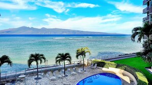 A poolside area with a view of the ocean and mountains. - Oceanfront Two-Bedroom With Large Lanai | Sunset Views, Pool + BBQ (Lahaina)