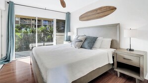 A bedroom with a bed, nightstand, ceiling fan, and a view of a balcony. - Oceanfront Two-Bedroom With Large Lanai | Sunset Views, Pool + BBQ (Lahaina)