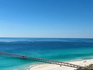Un molo si protende in un mare cristallino e blu, con una spiaggia sabbiosa all'estremità.