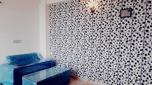 A room with a patterned wall, a blue sofa, and a glass coffee table. - Elegant 3-bedroom apartment in Rajawas (Rajawas)