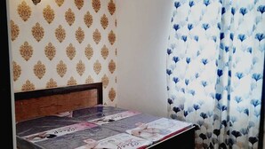 A bedroom with a bed, patterned wallpaper, a ceiling fan, and a window with curtains. - Elegant 3-bedroom apartment in Rajawas (Rajawas)