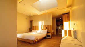 Una habitación de hotel moderna con una cama grande, un sofá y una cocina visible a través de una puerta abierta.