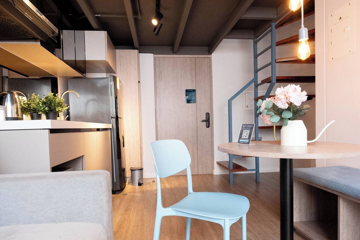 Een moderne keuken met een koelkast, gootsteen en potplanten. Er staat een blauwe stoel en een kleine tafel met een bloemenvaas.