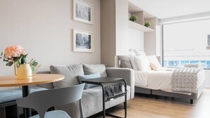 Ein modernes Wohnzimmer mit einer Couch, Sesseln, einem kleinen Tisch mit einer Vase und einem Bett mit Blick.