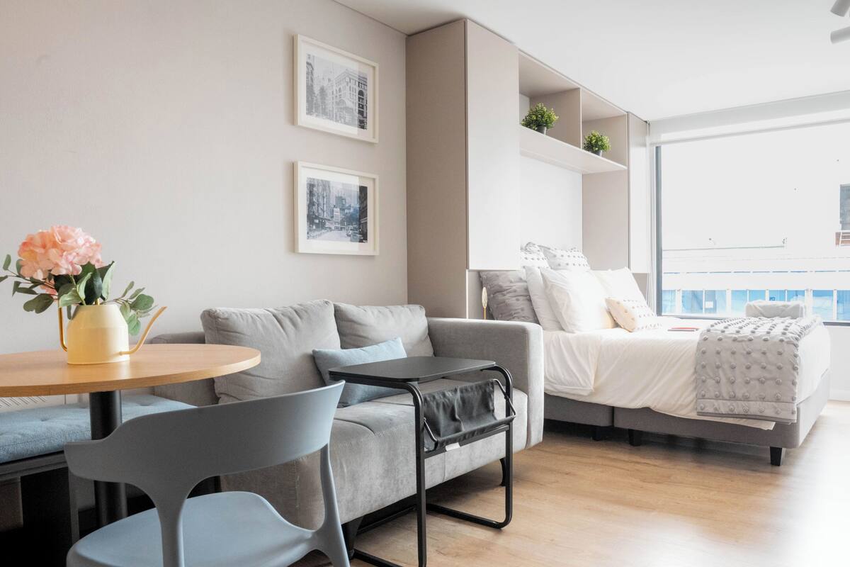 Een moderne woonkamer met een bank, stoelen, een klein tafeltje met een vaas, en een bed met uitzicht.