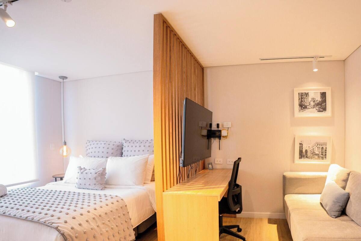 Een hotelkamer met een bed, een bureau, een televisie, een bank en twee ingelijste foto’s aan de muur.