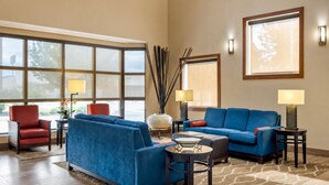 A hotel lobby with a blue sofa, red armchair, and a round coffee table. There are two lamps on side tables, a vase with plants, and a large window with a view. - Prime Baton Rouge Location Near LSU Museum, Zoo, and Riverfront Dining (Baton Rouge)