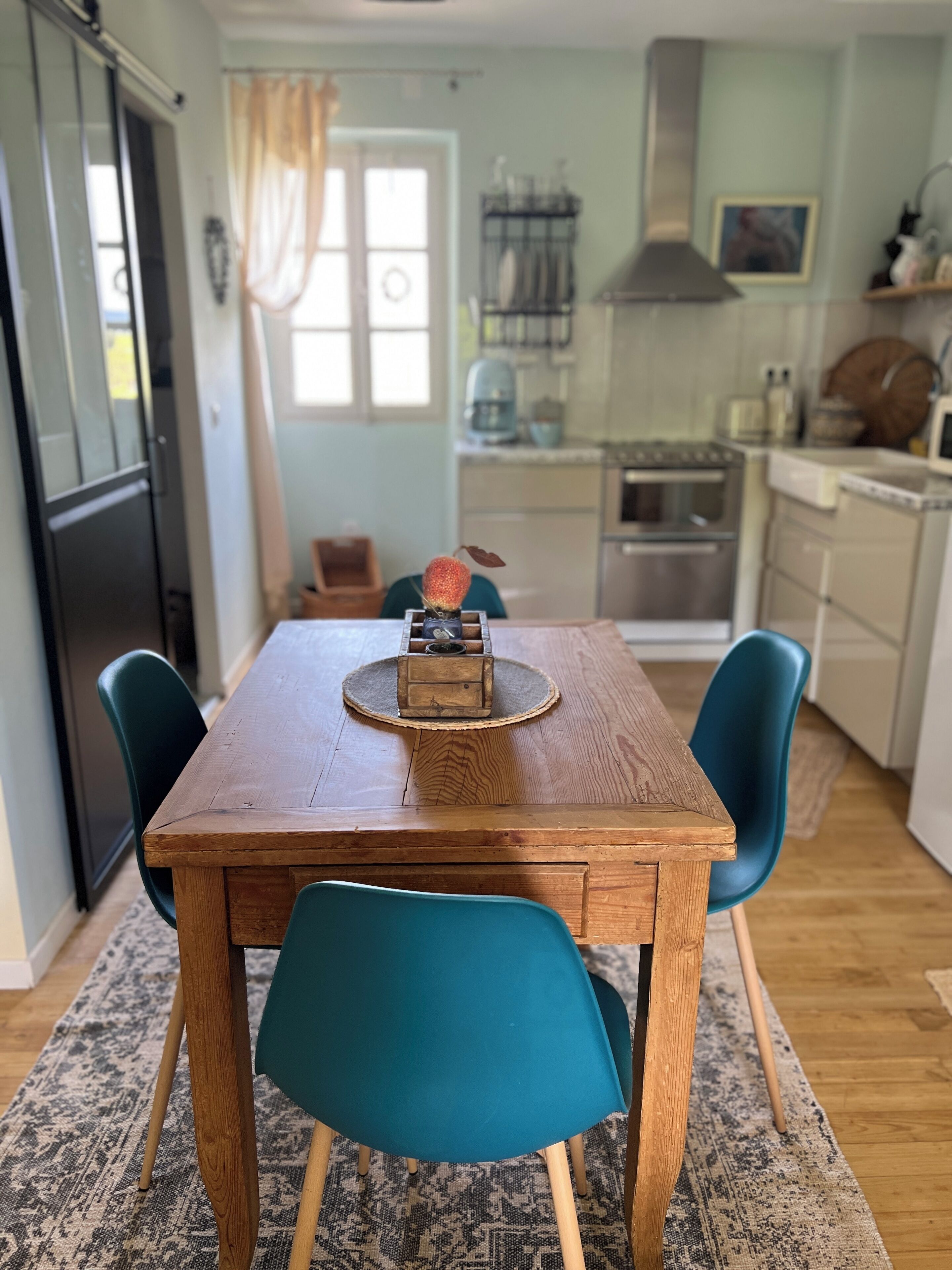 Un comedor con mesa de madera, sillas color turquesa y un centro de mesa decorativo.