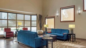 A spacious living room with a blue sofa set, a red armchair, and a coffee table. There are two lamps on side tables, and the room has large windows with a view outside. - Stay Near LSU & Tiger Stadium w/ Free Breakfast, Outdoor Pool, and Parking (Baton Rouge)