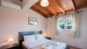 Une chambre d’hôtel avec un lit, des tables de chevet, un ventilateur de plafond, une fenêtre avec des rideaux et un tableau au mur.