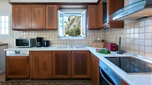Une cuisine avec des meubles en bois, un four à micro-ondes, une machine à café, un grille-pain et une fenêtre donnant sur les arbres.