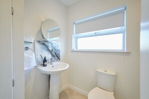 A bathroom with a white sink, a round mirror, a toilet, and a window with a blind. - Host & Stay | Prospect Retreat (Knaresborough)