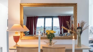 Ein Hotelzimmer mit einem großen Spiegel, einem Tisch mit Stühlen, einer Vase mit Blumen und Blick auf die Stadt durch das Fenster.