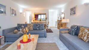 Ein modernes Wohnzimmer mit zwei grauen Sofas, einem Couchtisch mit Kerzen und einem Essbereich im Hintergrund.