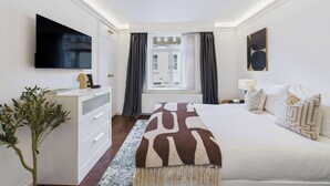 A hotel room with a bed, a TV, a dresser, a plant, and a window with curtains. - Elegant Marylebone Mews Apartment (Greater London)