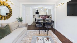 A modern living room with a sofa, a coffee table, and a dining area with chairs and a table. - Elegant Marylebone Mews Apartment (Greater London)