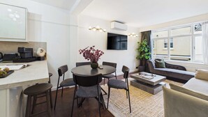 A modern living room with a round dining table, grey upholstered chairs, a sofa, and a large window with curtains. - Elegant Marylebone Mews Apartment (Greater London)