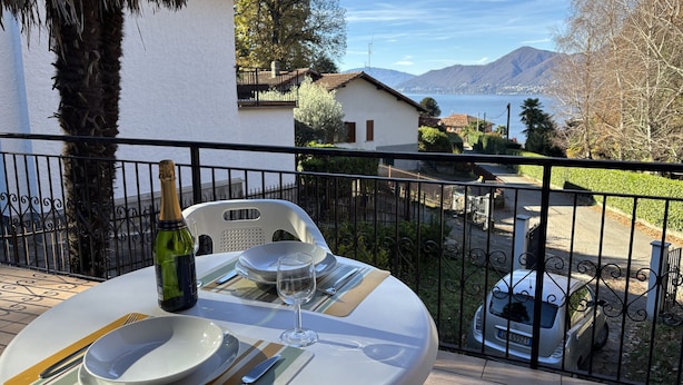A table set for two with a bottle of wine and a glass, overlooking a scenic view of mountains and a body of water. - Carmen apartment with lake view and balcony (Luino)