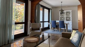 A modern living room with a glass coffee table, two sofas, and a dining area with blue chairs. - Carmen apartment with lake view and balcony (Luino)
