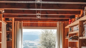 Ein Holzinnenraum mit Tisch, Bänken, Küchenutensilien auf Regalen und einem Fenster mit Blick auf einen See und Berge.