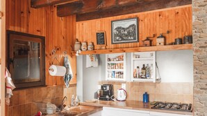 Eine kompakte Küche mit Holzbalken, weißen Schränken, einer Wand aus Naturstein und einem kleinen Fenster.