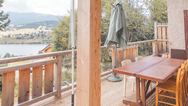 Eine Holzterrasse mit Tisch und Stühlen mit Blick auf einen See und Berge.