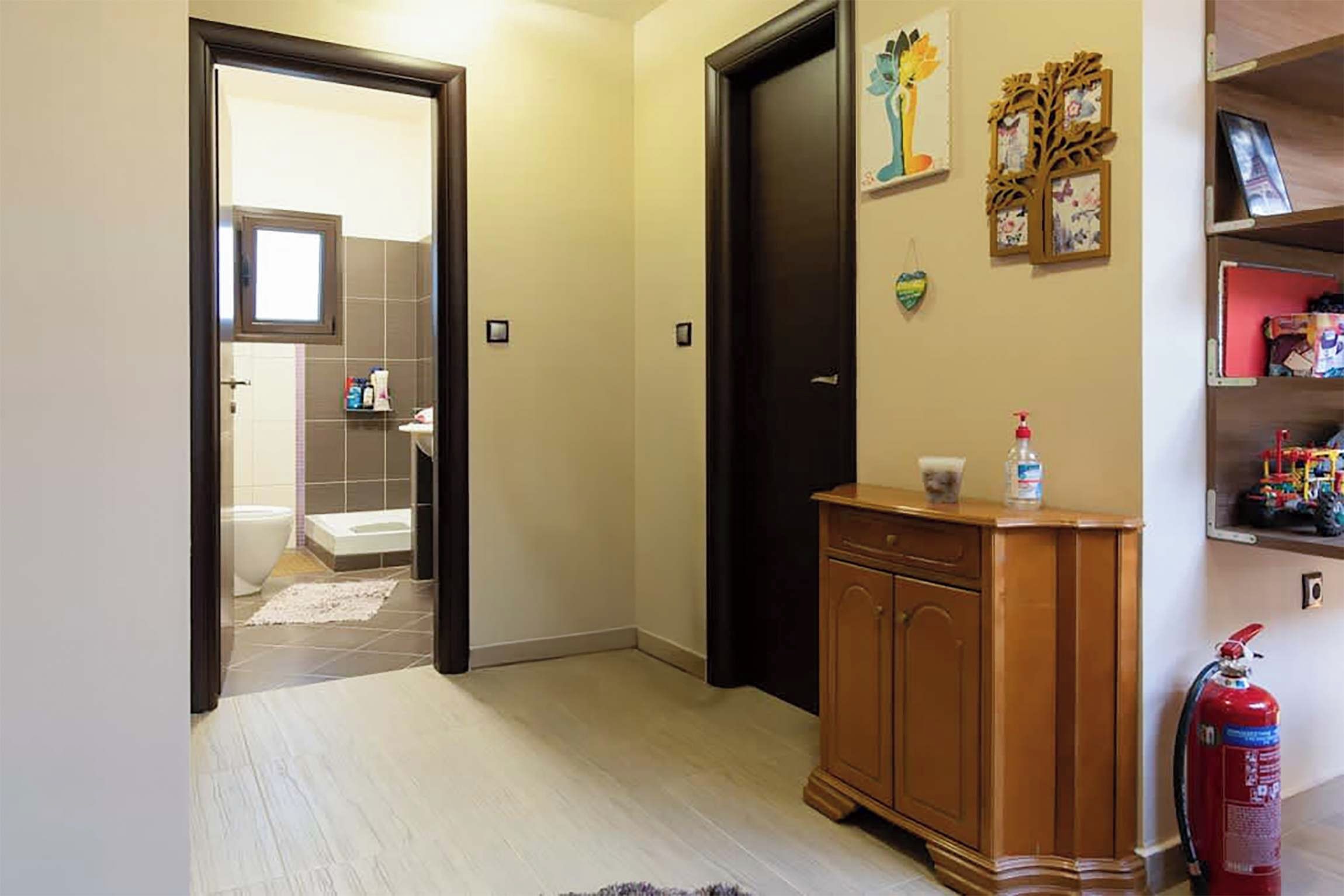 Een gang met een houten kast, een brandblusser en een deur naar een badkamer.