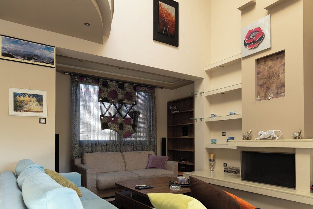 A living room with a sofa, a coffee table, and a fireplace. There are framed pictures on the walls and a window with patterned curtains.