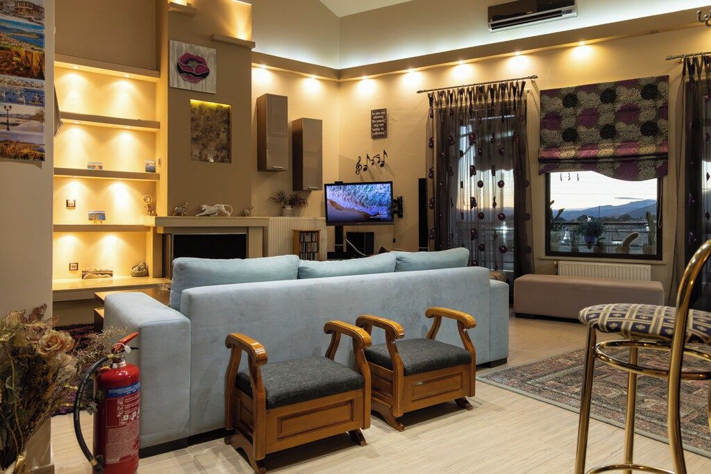 Een woonkamer met een bank, twee houten stoelen, een televisie en een open haard.