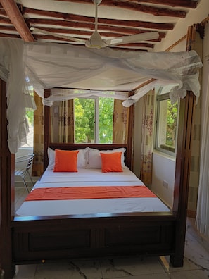 Ein Bett mit weißer und orangefarbener Bettwäsche, einem Holzkopfende und einem Baldachin.