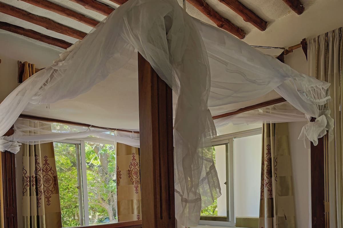A four-poster bed with a canopy, wooden headboard, and a white and orange bedspread.