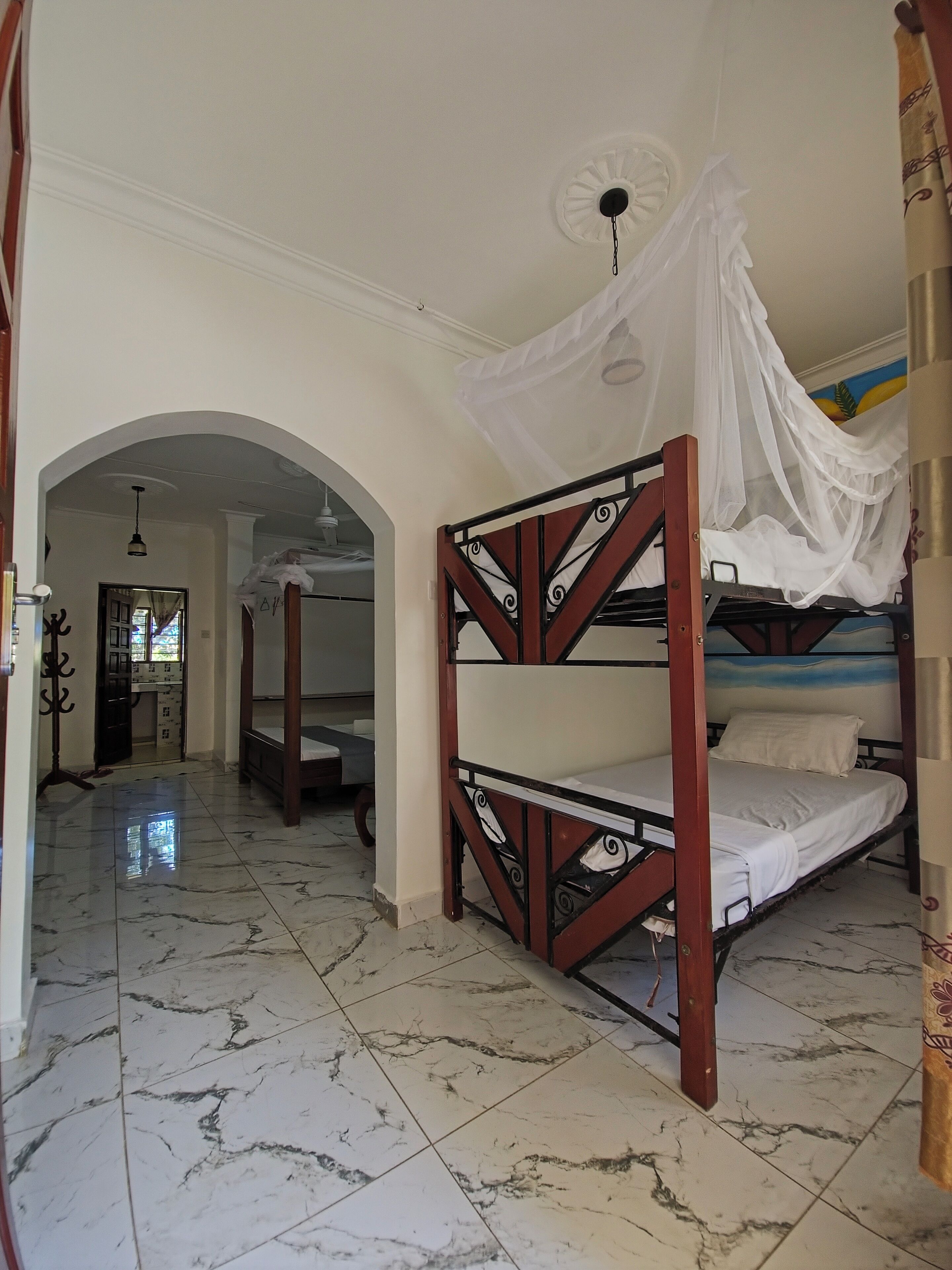 A room with a bed under a canopy, a tiled floor, and a hallway leading to another room.