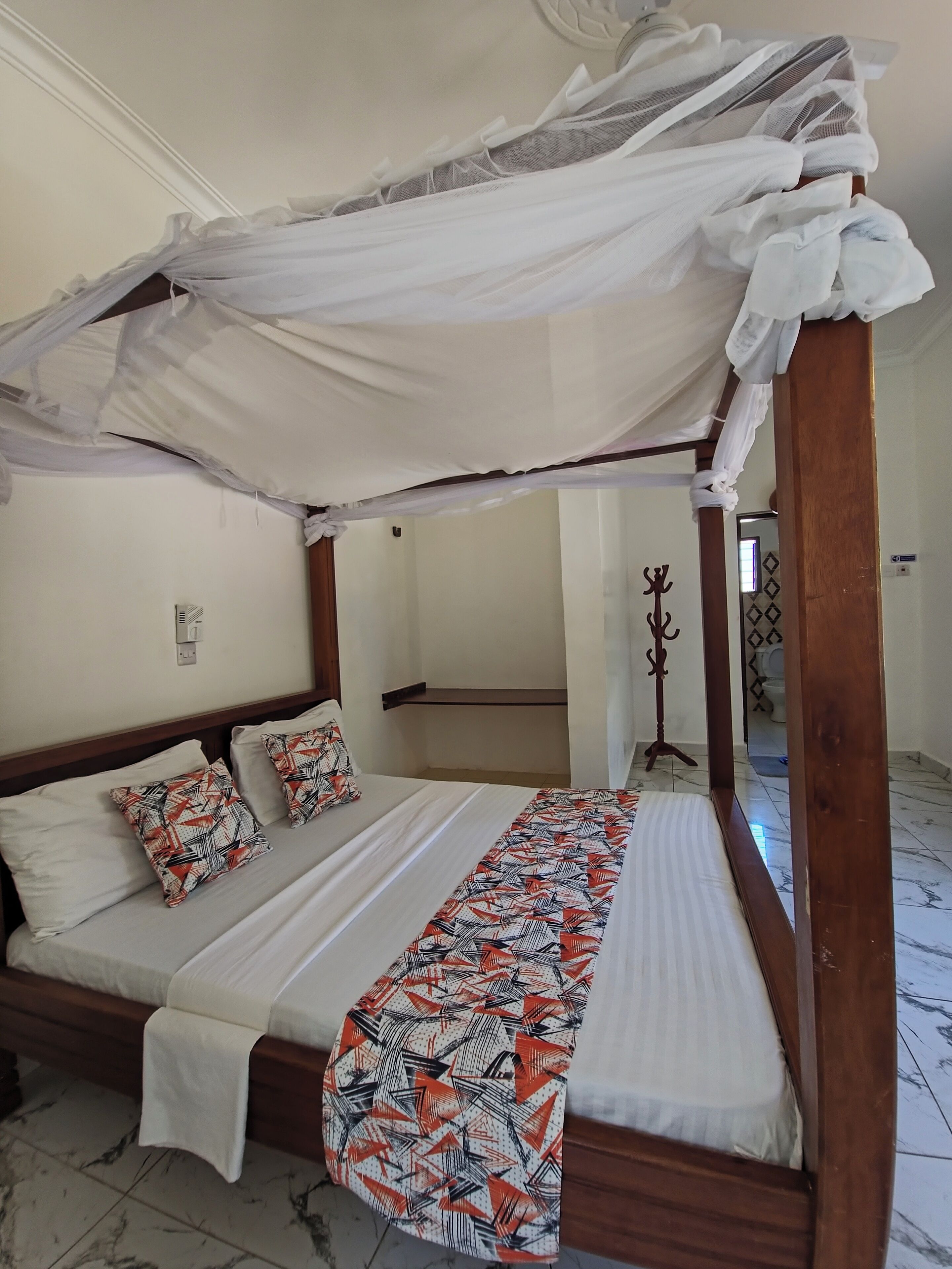 Een hemelbed met een wit sprei en twee kussens met een patroon.