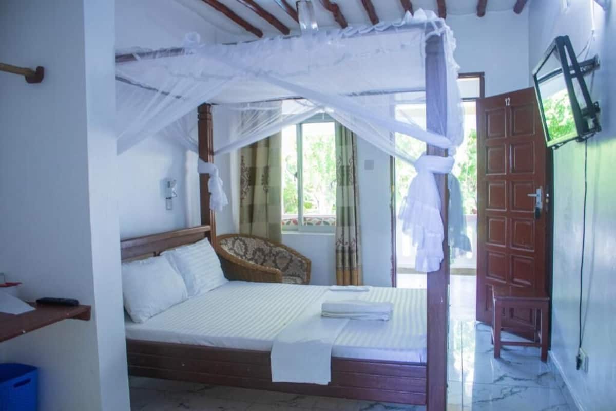 A room with a bed, a wooden headboard, a window with curtains, a door, and a television mounted on the wall.