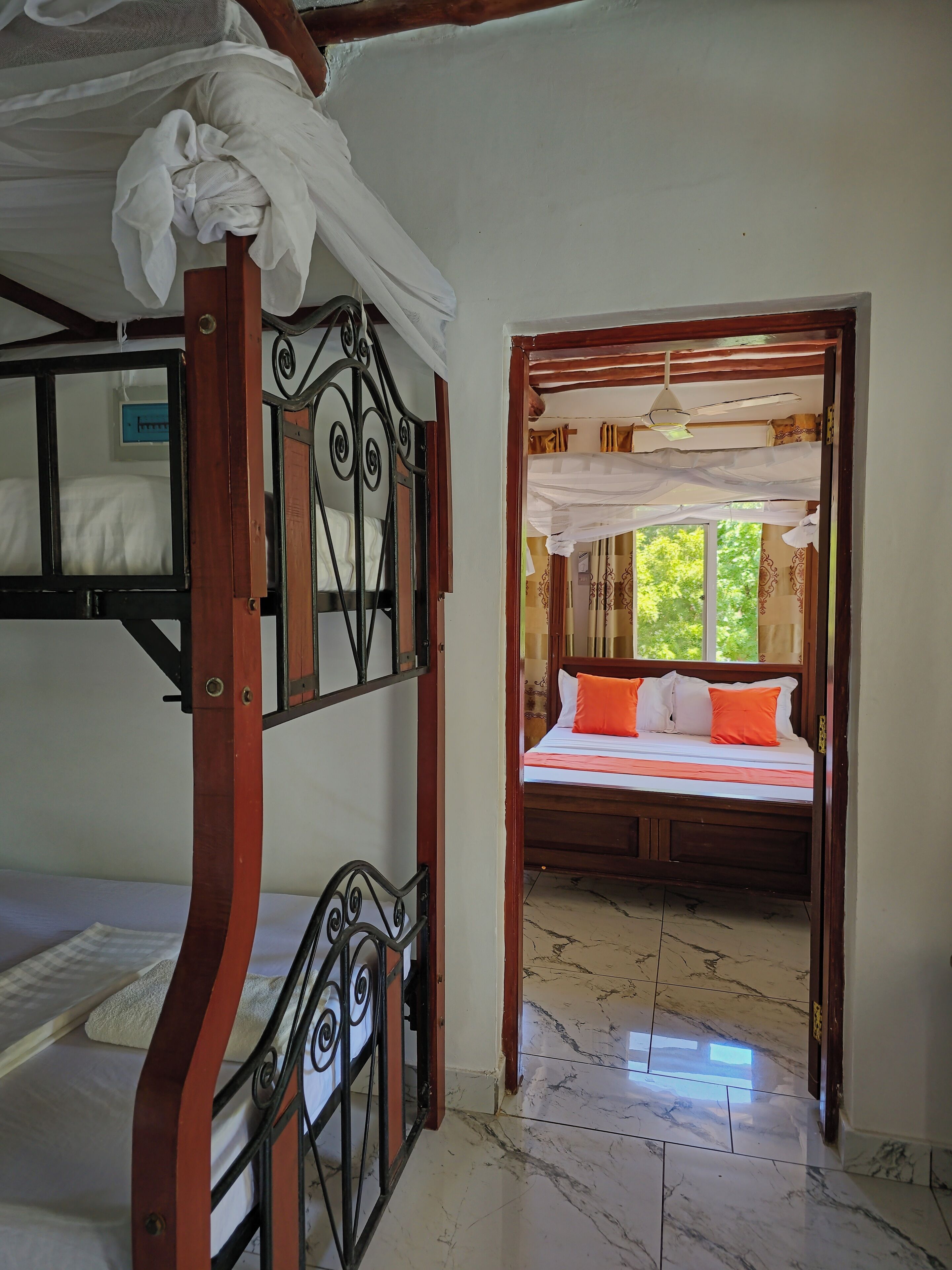 Une chambre avec un lit superposé, un lit simple avec des oreillers orange et une vue sur l’extérieur par une porte.