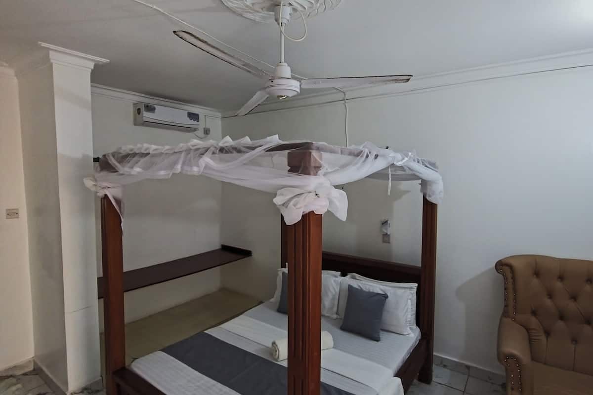 A room with a four-poster bed, a ceiling fan, a brown armchair, and a marble-tiled floor.